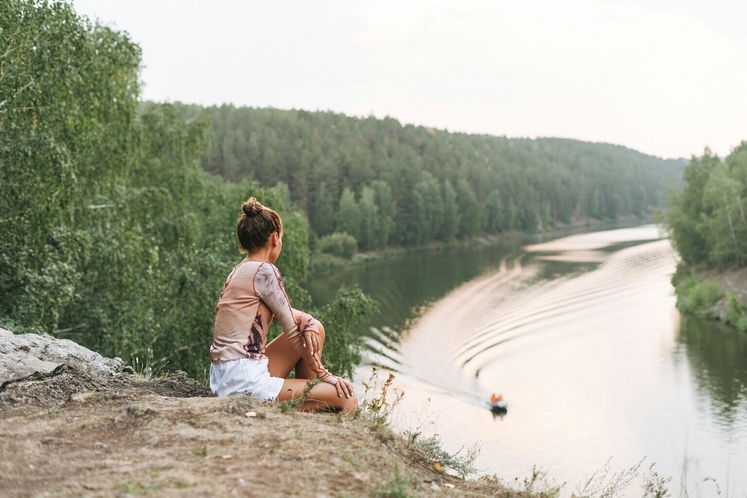 Person sitzt auf einem Felsen über einem Fluss und blickt in die Landschaft
